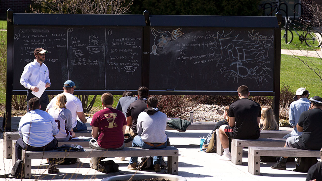 Professor lecturing to a group of students in an outdoor classroom 