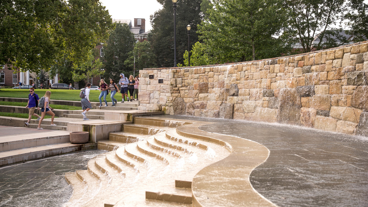 Closeup of the tiered fountain in alumni plaza with students climbing the nearby stairs in the background 
