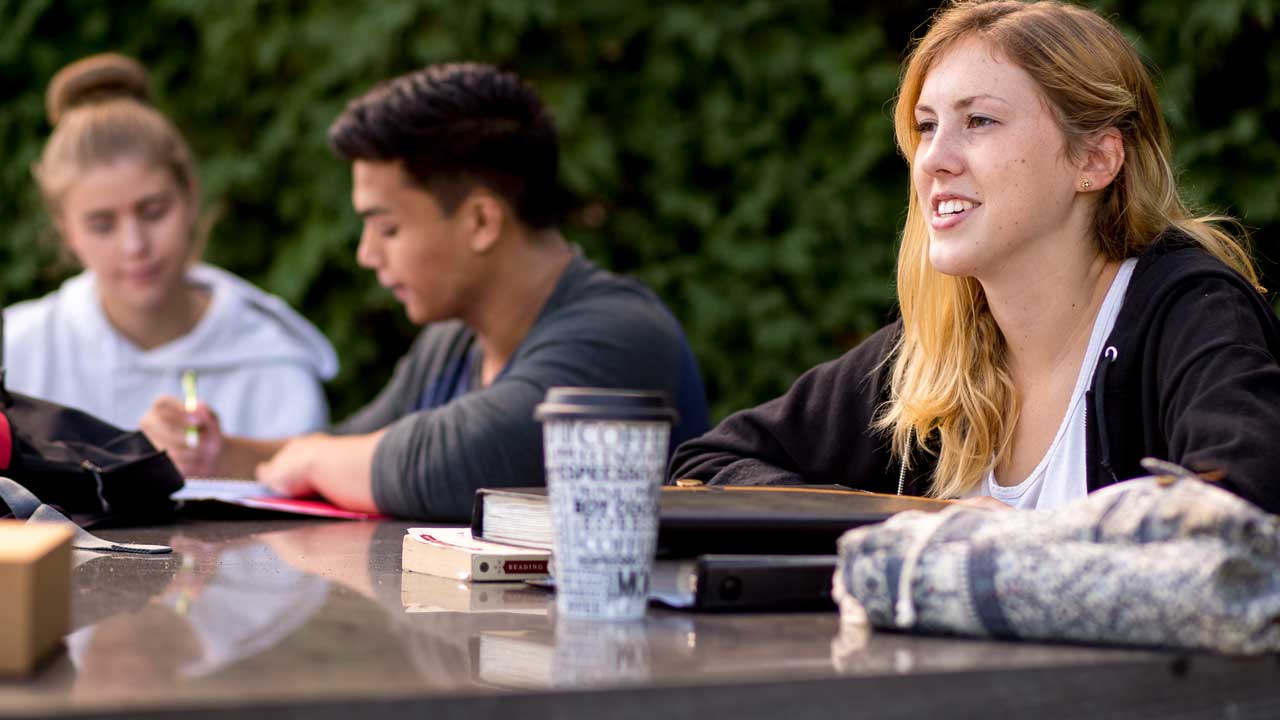 Three students, one female in the foreground, another male and female in the background study in the outdoor classroom on campus of kutztown university